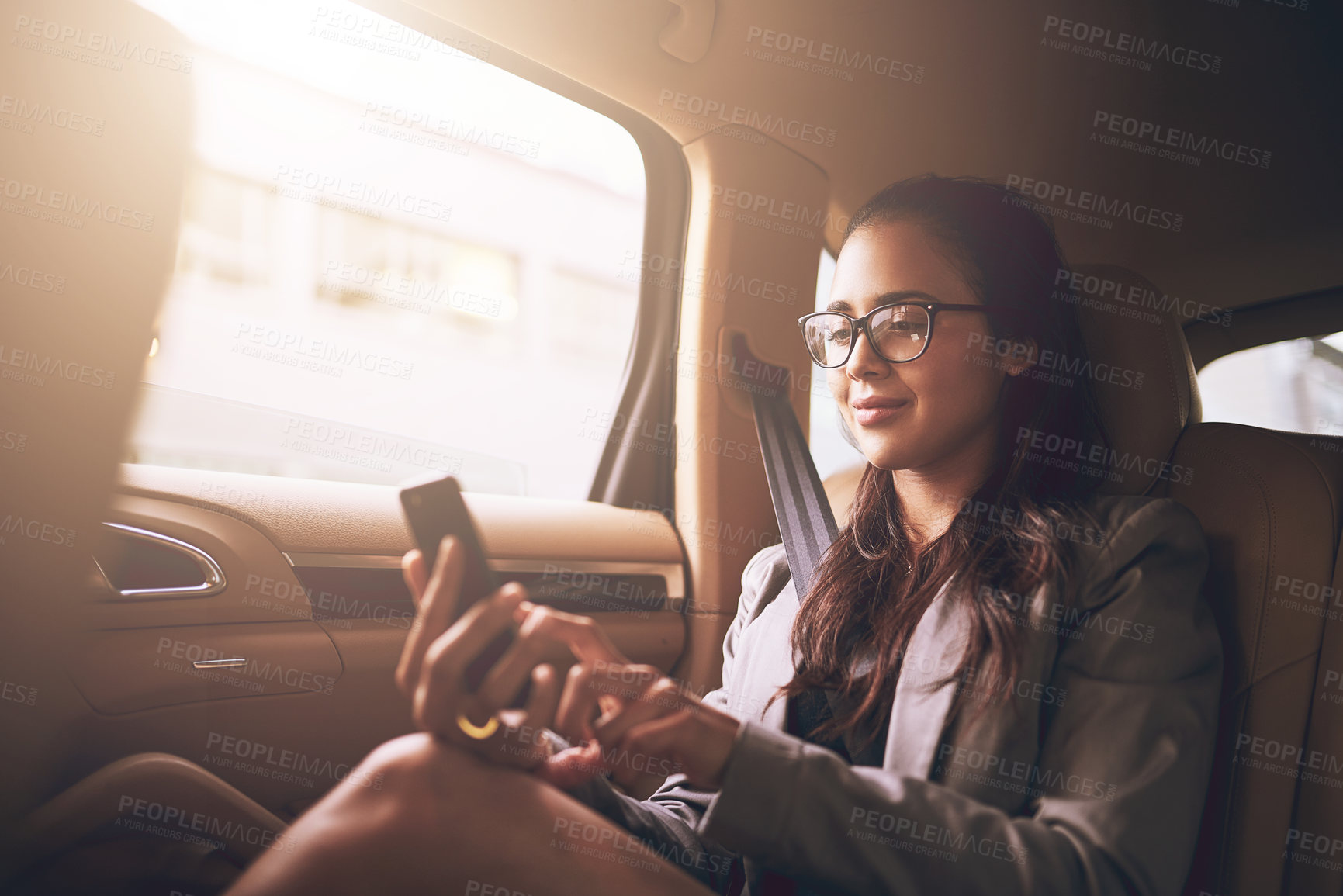 Buy stock photo Shot of a young businesswoman texting on a cellphone in the backseat of a car