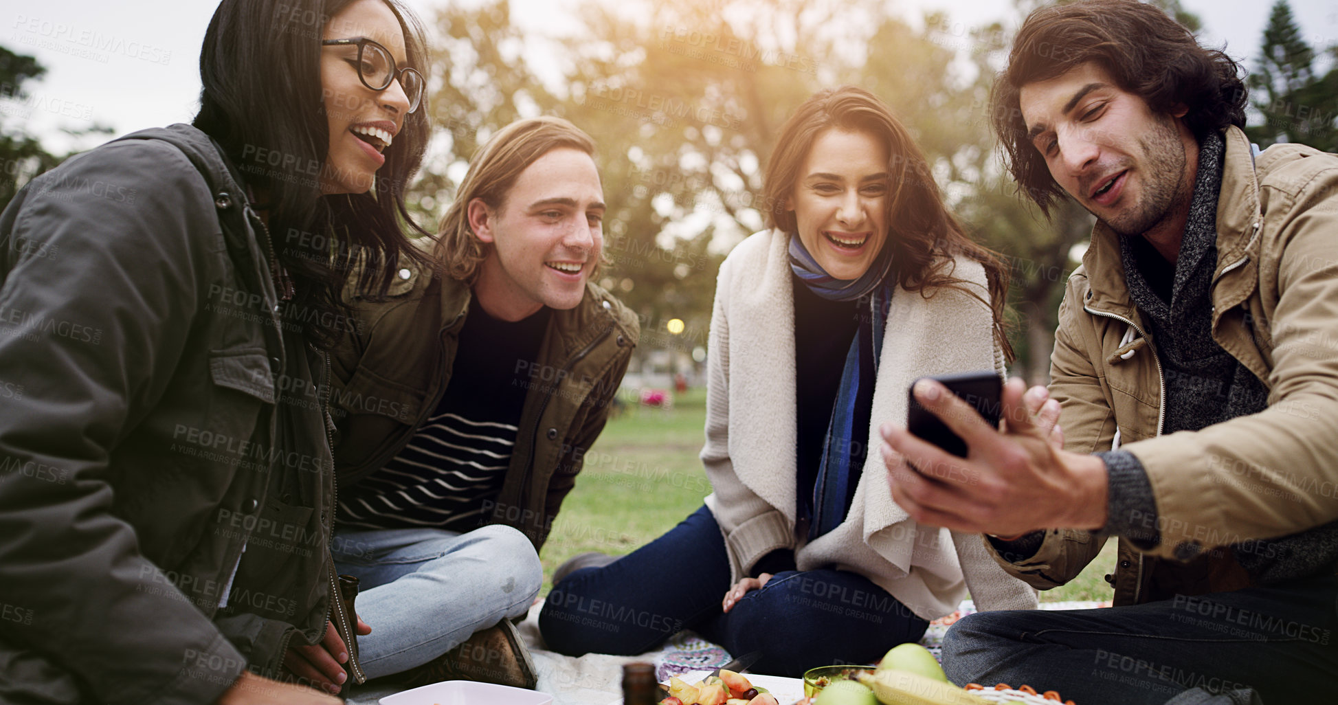 Buy stock photo Friends, phone and conversation in park for picnic, bonding and relax on weekend with snacks in summer. Group of people, mobile and talking outdoor for reunion, internet and social media on blanket