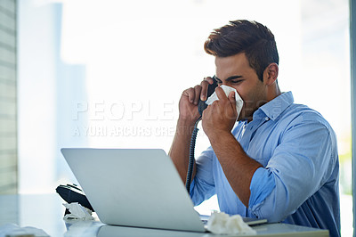 Buy stock photo Shot of a young businessman blowing his nose while talking on a phone in an office