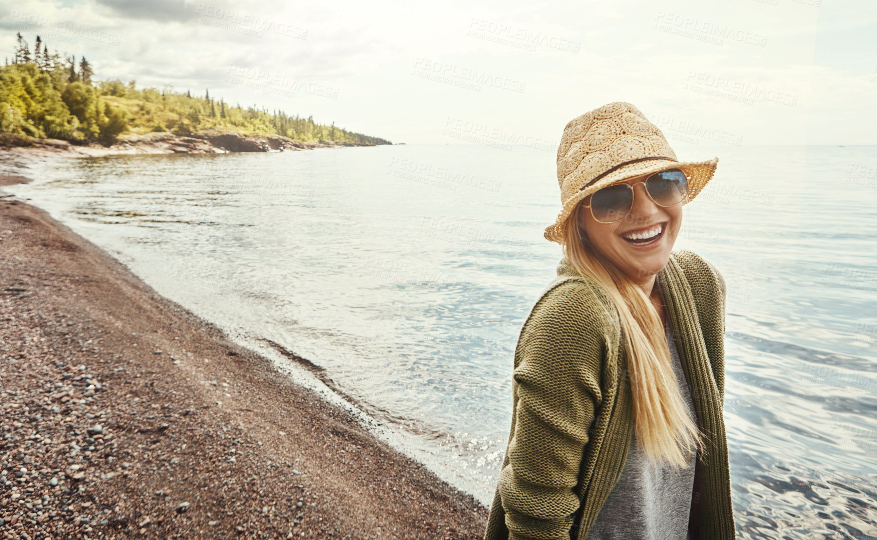 Buy stock photo Happy woman, portrait and laughing with hat at beach for holiday, weekend or outdoor getaway. Young female person with smile or glasses for fun journey, trip or happiness by ocean coast in nature