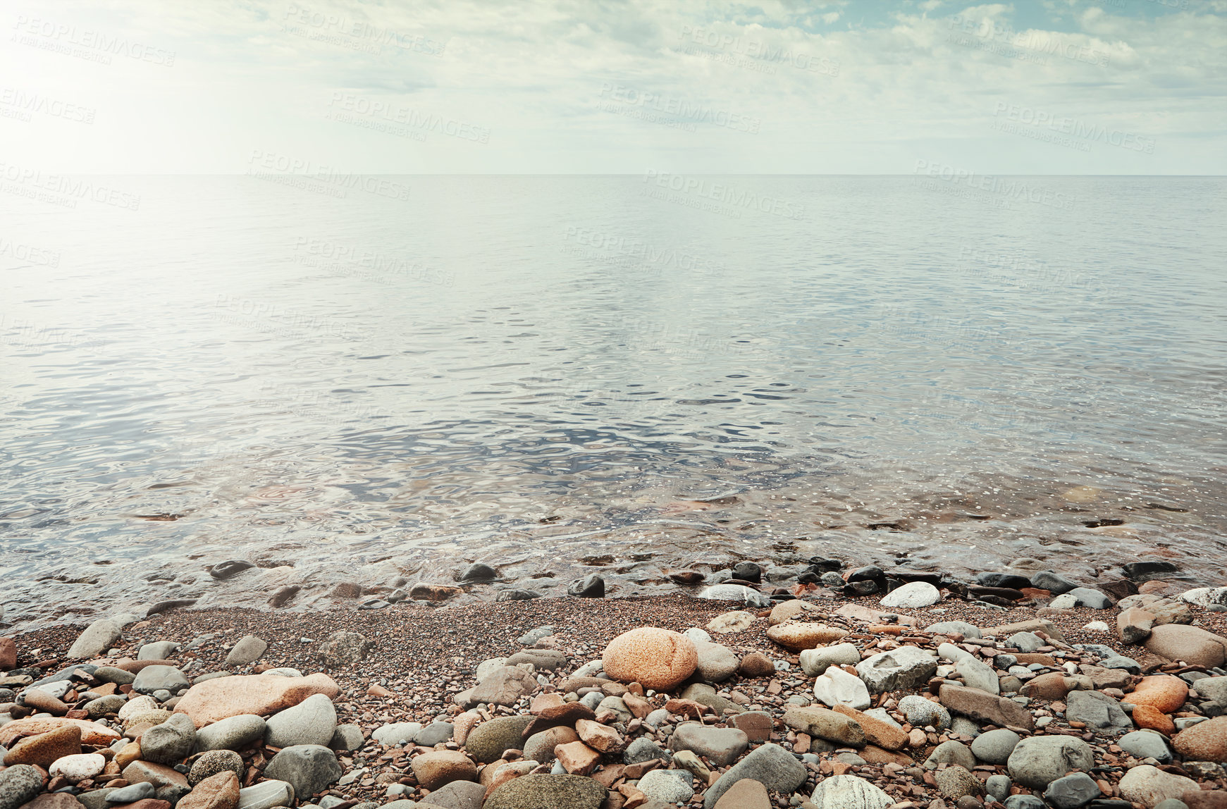 Buy stock photo Outdoor, water and peace at ocean with pebbles, tranquil and calm environment for natural ecosystem. Space, serene landscape and stones at sea with ecology, scenery and sustainability for nature.
