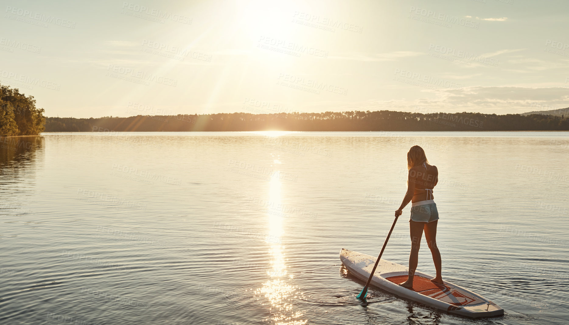 Buy stock photo Lake, sunset and woman on paddle board for relax, water sports and vacation on river for tourism. Sunshine, summer and holiday in Germany for female person, swimsuit and back fitness for adventure
