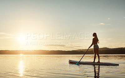 Buy stock photo Lake, sunshine and woman on paddle board for water sport, forest and vacation on river for tourism. Exercise, sunset and holiday in Germany for female person, view and travel fitness for adventure