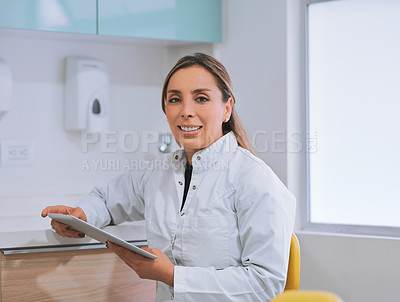 Buy stock photo Portrait of a cheerful young  female dentist working on her digital tablet while looking at the camera in her office