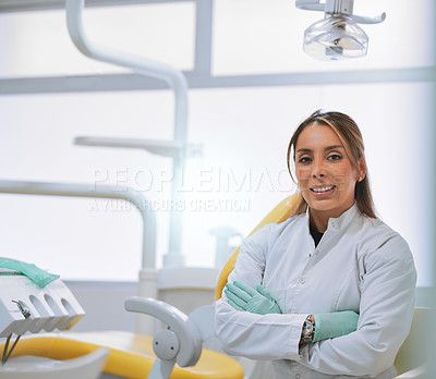 Buy stock photo Portrait of a cheerful young female dentist standing with her arms folded while looking at the camera in her office