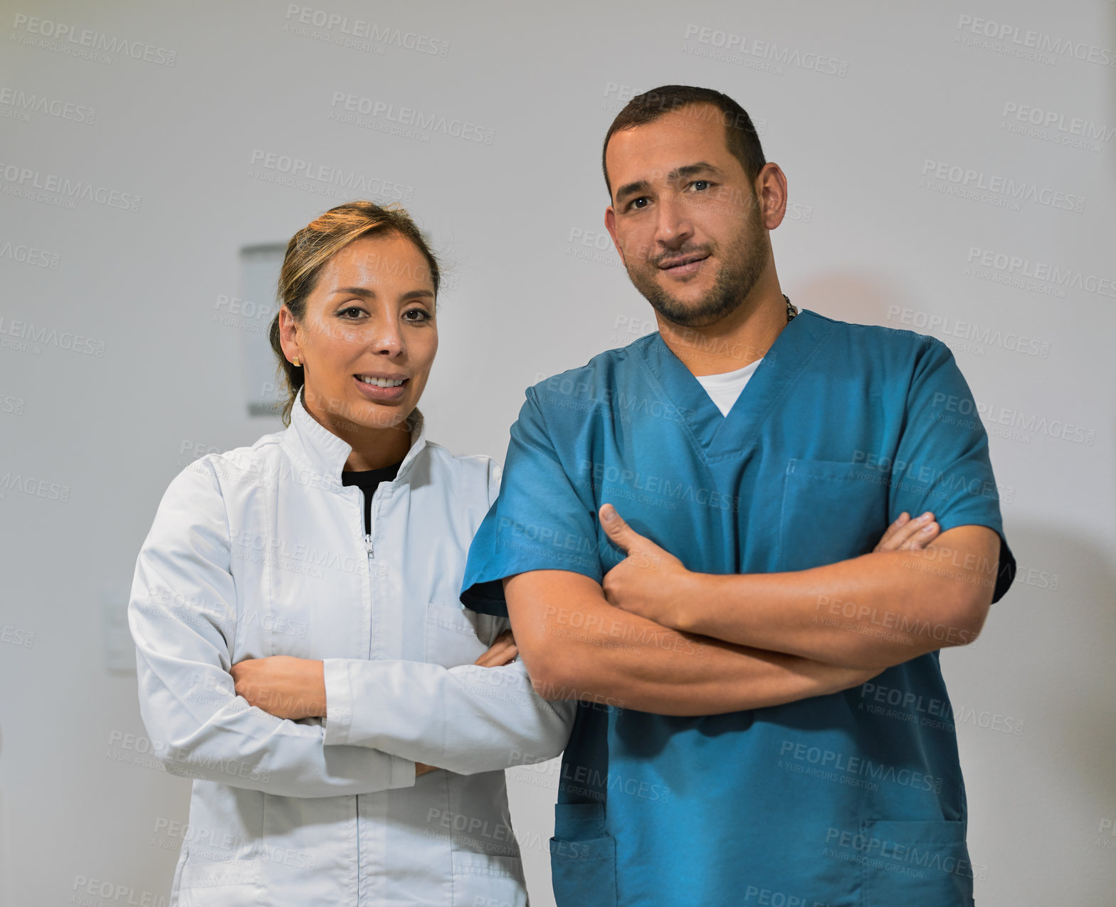 Buy stock photo Shot of two confident young dentists standing with arms folded while looking into the camera inside the office