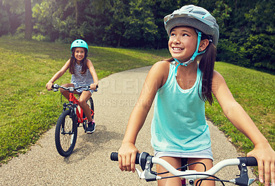 Buy stock photo Shot of two young girls out for a bicycle ride in the park