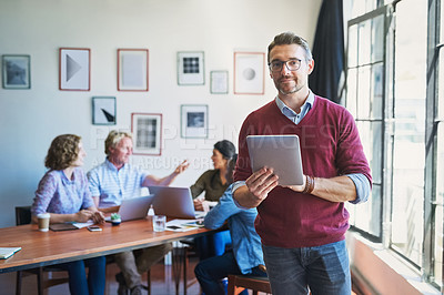 Buy stock photo Shot of a mature man using a digital tablet with his team in the background of a modern office shot of entrepreneurs meeting in the boardroom
