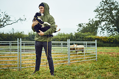 Buy stock photo Shot of a cheerful young farmer holding his young little sheepdog puppy in his arms outside during the day