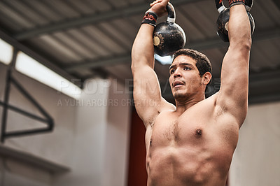 Buy stock photo Shot of a young man lifting kettlebells in a gym