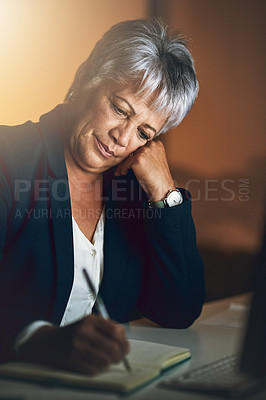 Buy stock photo Shot of a mature businesswoman writing in a notebook during a late night at work