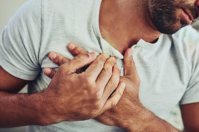 Buy stock photo Shot of a unrecognisable young man holding his chest in discomfort with his hands due to pain in that area