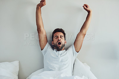 Buy stock photo Shot of a tired young man waking up after a good night's sleep while putting is arms in the air and yawning