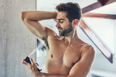 Buy stock photo Shot of a cheerful young man without a shirt spraying deodorant under his one armpit in the bathroom