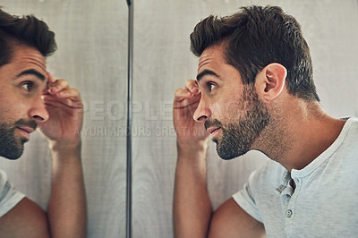 Buy stock photo Shot of a confident young man looking at himself closely in the mirror at home during the day