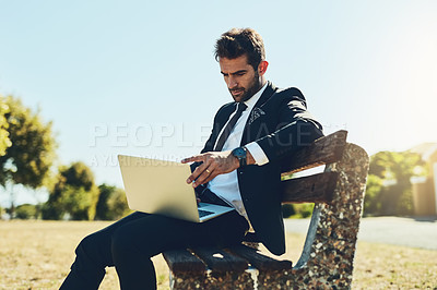 Buy stock photo Cropped shot of a handsome young corporate businessman using a laptop at a public park