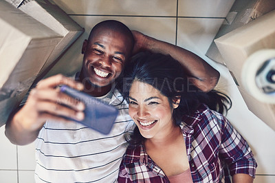 Buy stock photo High angle shot of a young couple taking a selfie in their new home