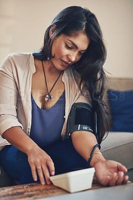 Buy stock photo Shot of a young woman checking her blood pressure at home