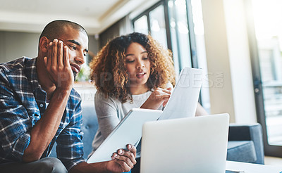 Buy stock photo Black couple talking, reading finance papers and planning their bills while working on tablet and laptop on the couch together at home. Husband and wife going through paperwork for tax and loans