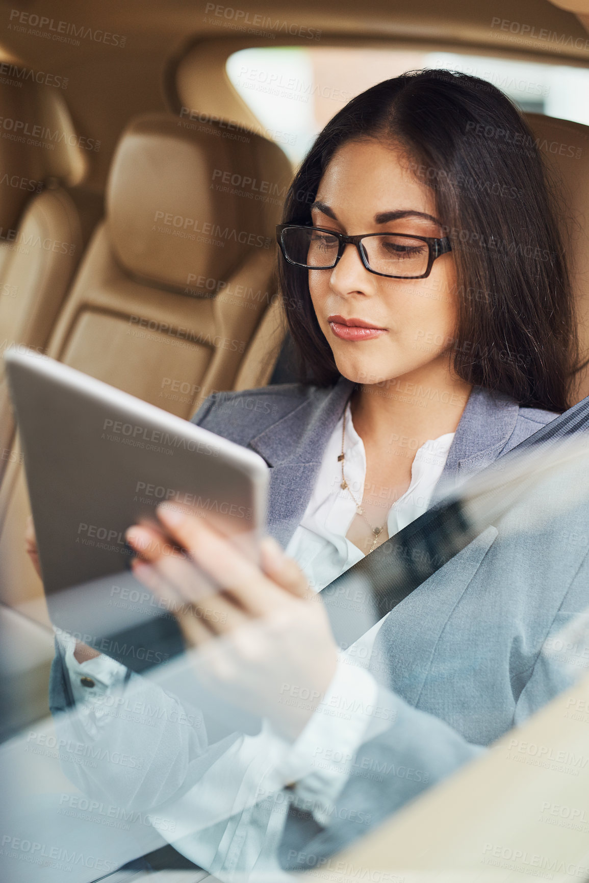 Buy stock photo Shot of a young businesswoman using her digital tablet while sitting in the backseat of a car