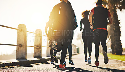 Buy stock photo Rearview shot of a fitness group out running on the promenade