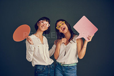 Buy stock photo Studio shot of two cheerful young women holding up speech bubbles while standing against a dark background