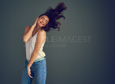 Buy stock photo Studio shot of a carefree young woman holding her face while her hair gets blown by wind against a dark background