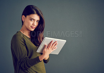 Buy stock photo Studio shot of an confident young woman holding a digital tablet while standing against a dark background