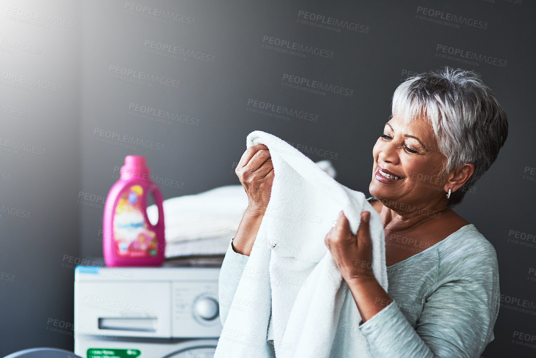 Buy stock photo Shot of a mature woman smelling freshly washed towels while doing laundry at home