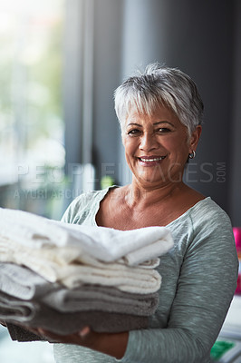Buy stock photo Portrait of a mature woman holding freshly folded towels while doing laundry at home
