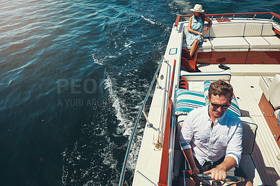 Buy stock photo High angle shot of a handsome young man steering a yacht with his wife sitting in the background