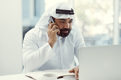 Buy stock photo Cropped shot of a young businessman dressed in Islamic traditional clothing using his cellphone while working in his office