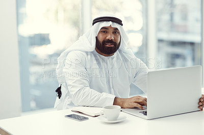 Buy stock photo Cropped portrait of a young businessman dressed in Islamic traditional clothing working on his laptop while sitting in the office