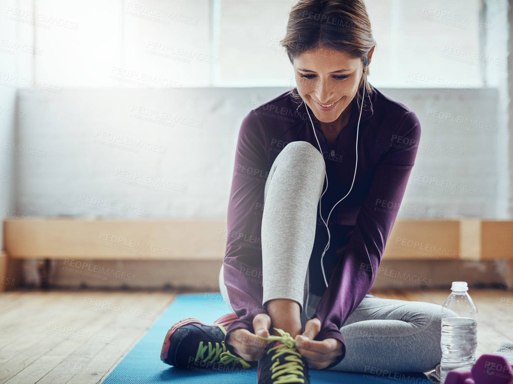 Buy stock photo Shot of an attractive young woman tying her shoelaces while working out at home