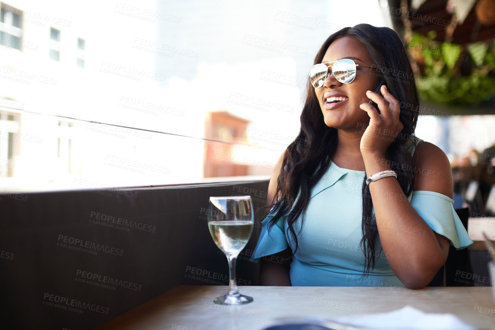 Buy stock photo Shot of a cheerful young woman talking on her phone while enjoying a glass of wine at a restaurant during the day