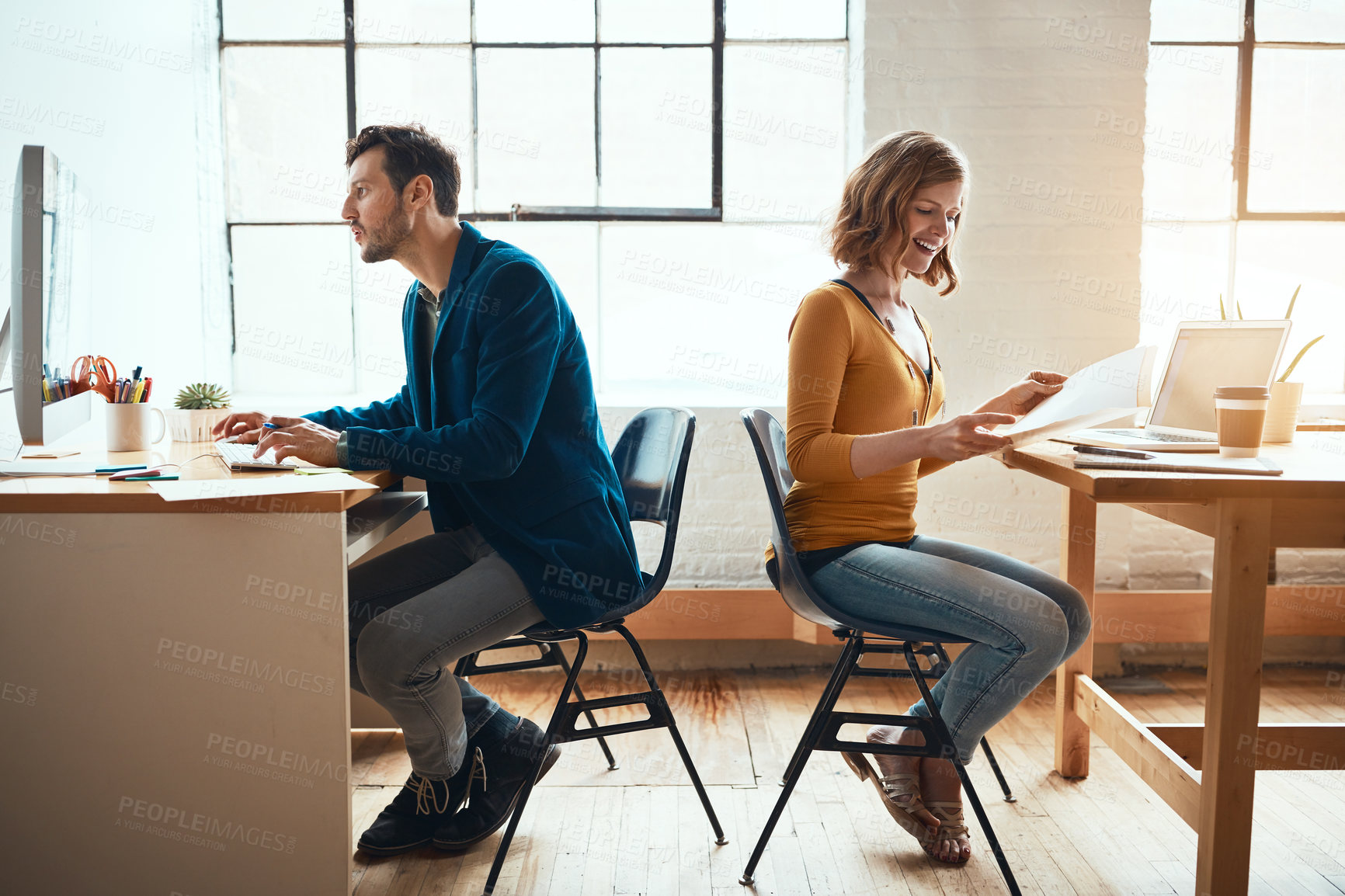 Buy stock photo Full length shot of two young businesspeople working back to back in a modern office