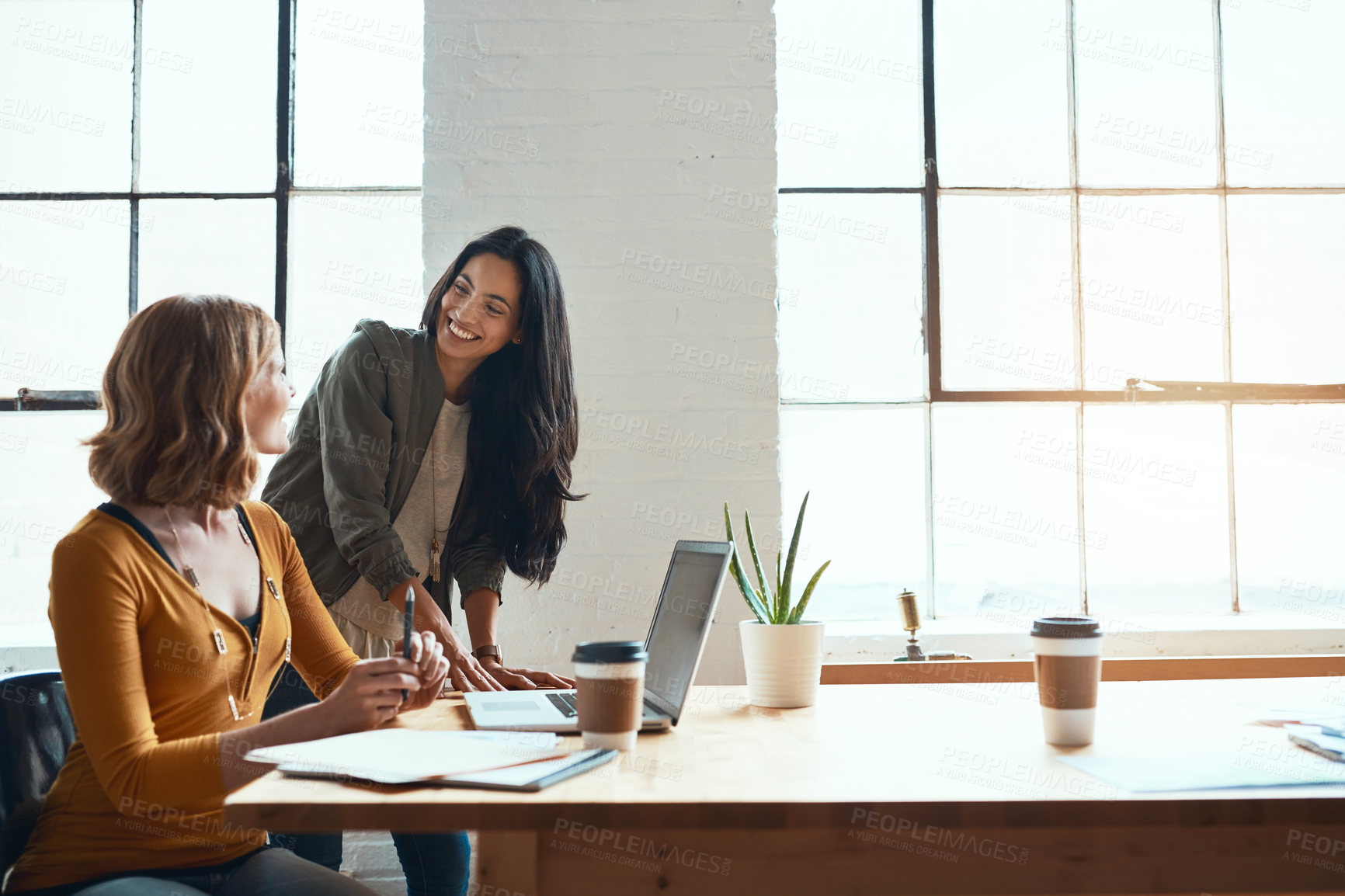 Buy stock photo Cropped shot of two young businesswomen working on a laptop together in their modern office