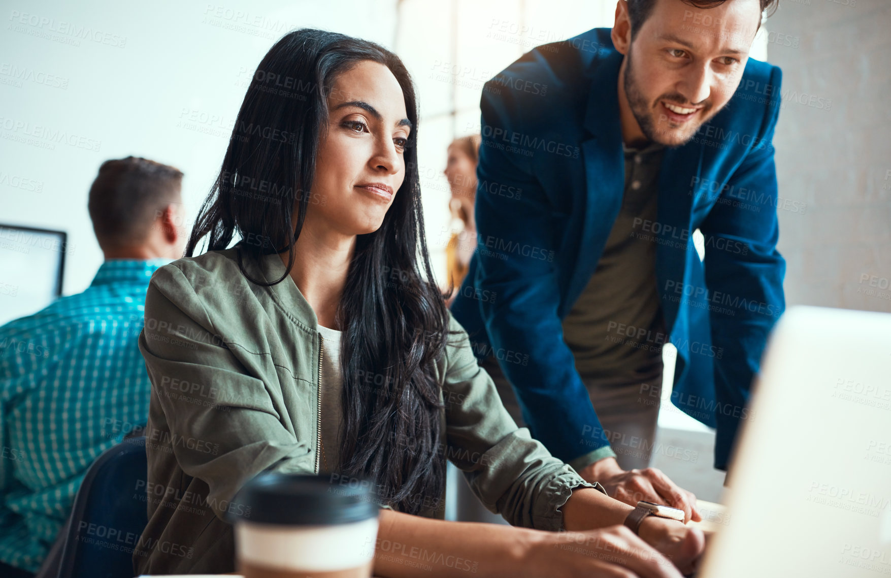 Buy stock photo Shot of two young business colleagues working together in a modern office with their colleagues in the background