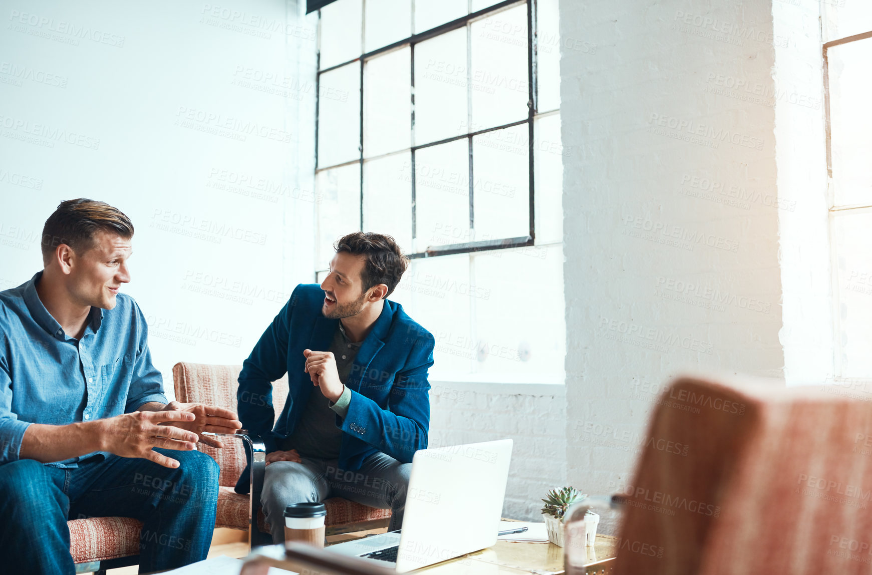 Buy stock photo Shot of two young businessmen having a discussion and using a laptop together in a modern office