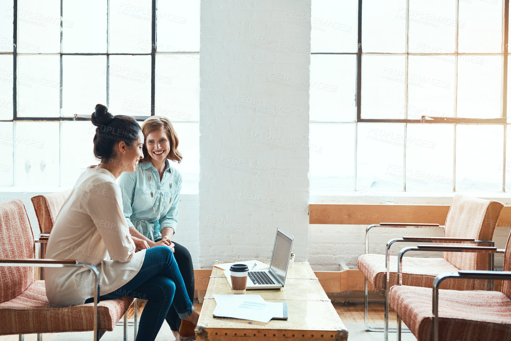 Buy stock photo Shot of two young businesswomen discussing paperwork in a modern office