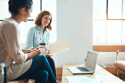 Buy stock photo Shot of two young businesswomen discussing paperwork in a modern office