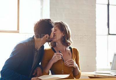 Buy stock photo Cropped shot of young couple kissing while working together in their modern office