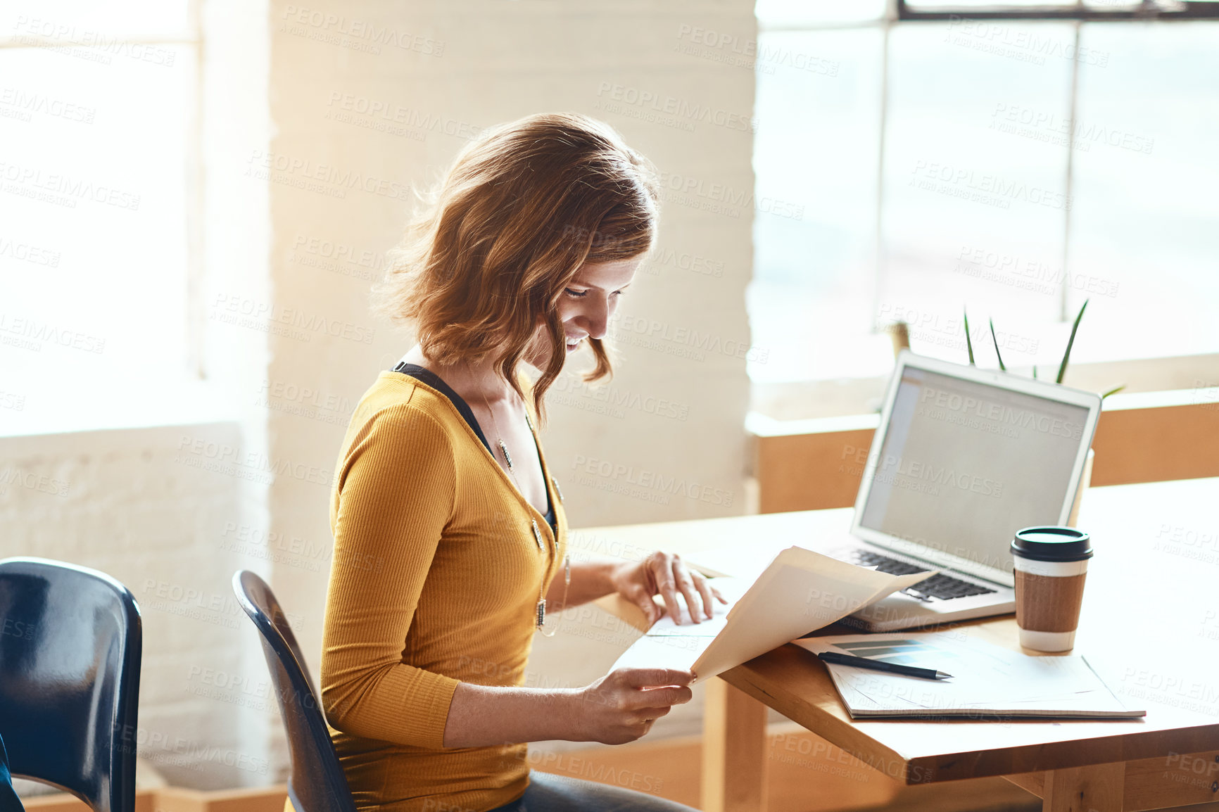 Buy stock photo Cropped shot of an attractive young woman looking over some paperwork while working in a modern office