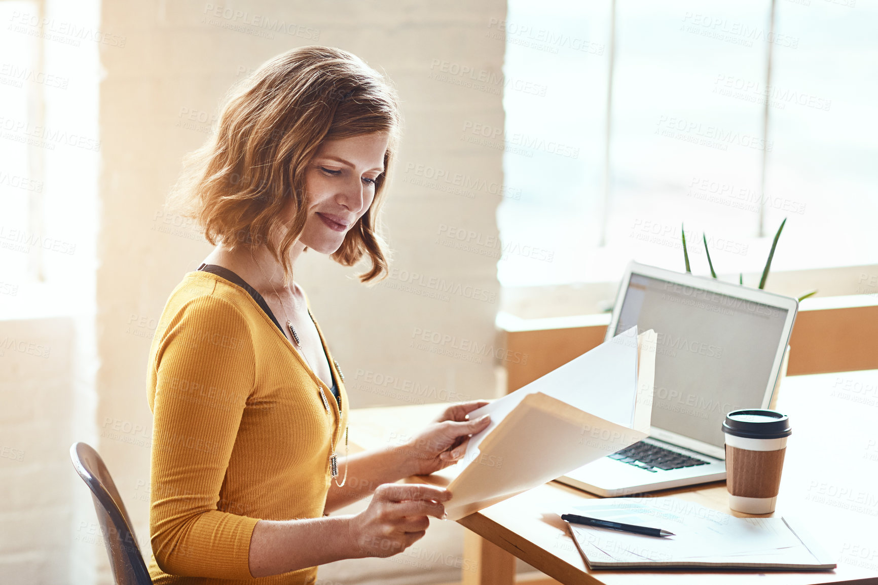 Buy stock photo Cropped shot of an attractive young woman looking over some paperwork while working in a modern office