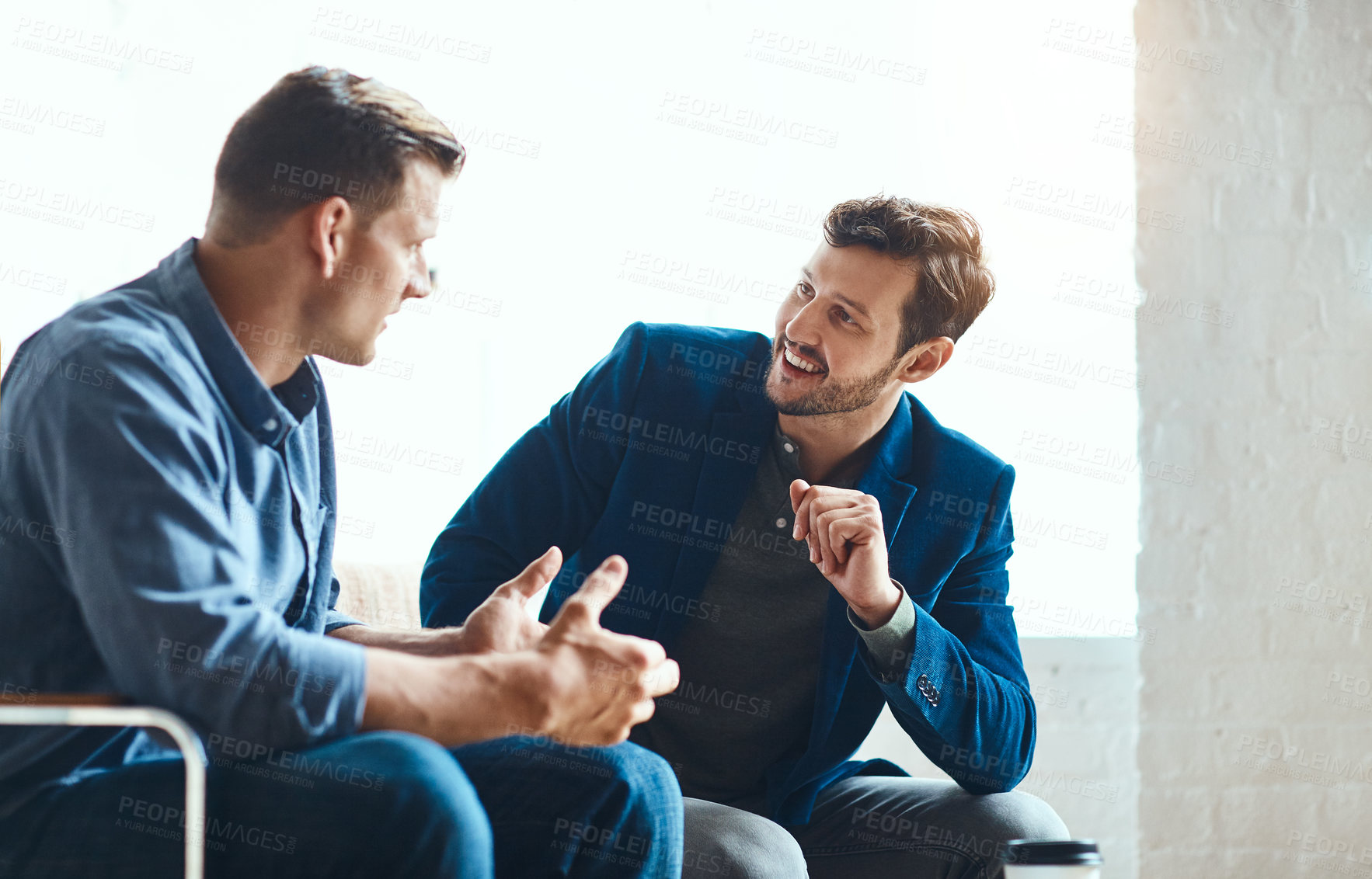 Buy stock photo Cropped shot of two young businessmen chatting while working together in their modern office