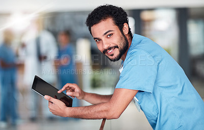 Buy stock photo Portrait of a cheerful young doctor browsing on a digital tablet while standing in a hospital during the day