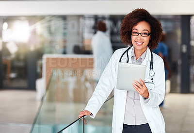 Buy stock photo Shot of a cheerful young doctor browsing on a digital tablet while standing in a hospital during the day