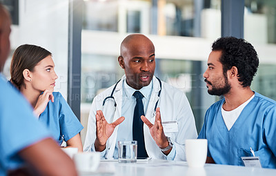 Buy stock photo Shot of a group of focused young doctors having a discussion together while being seated in a hospital