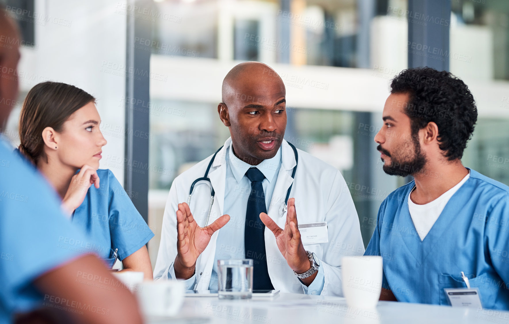 Buy stock photo Shot of a group of focused young doctors having a discussion together while being seated in a hospital