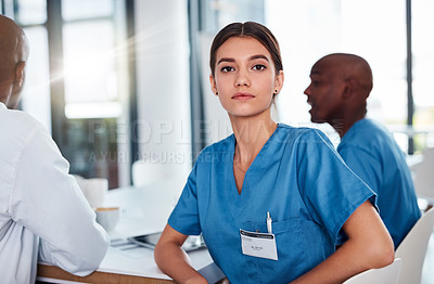 Buy stock photo Portrait of a focused young doctor seated at a table during a meeting inside of a hospital during the day